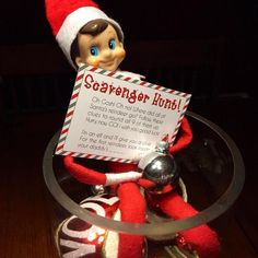 an elf with a sign in his hand sitting on top of a christmas ornament