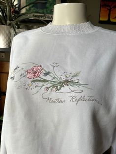 This crewneck sweater is perfect for the cottage or sitting in a rocking chair with a kitty in your lap. It features a flower graphic on white with a pink embroidered flower as the centrepiece. Signed with the Northern Reflections brand and a knit crew neckline resembling crochet as an added touch.  Label: Northern Reflections Made in Canada Size: Medium Measurements (taken flat): Pit to pit - 22" Hem - 17" Shoulder to hem - 24.5" Pit to hem - 13" Good vintage condition - there are a few stains, White Pullover, Flower Graphic, Crewneck Sweater, Embroidered Flowers, Rocking Chair, Floral Embroidery, Crew Neck Sweater, Crew Neckline, Sweatshirts Women