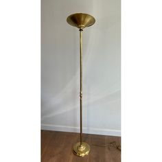 an antique brass floor lamp in the shape of a cone on a wooden floor with a white wall behind it