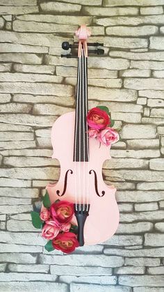 a pink violin with flowers on it is hanging from the wall next to a brick wall