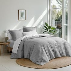 a bedroom with a large window and a bed covered in grey linens, along with a rug on the floor