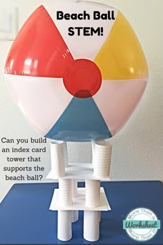 an inflatable beach ball is sitting on top of a table with the caption, can you build an index card tower that supports the beach ball?