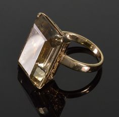 Eye catching 18K gold cocktail ring with eye clean large emerald cut smoky quartz gem of great color. The ring size is 8 1/2. The emerald cut smoky quartz is 22 mm X 16 mm, approx 8 mm deep, calculated 22.3 ct weigh. It is set in the high intricately cut open work crown. The long sides designed as floral scroll work, the short sides also have a witch heart and a card diamond suit. The ring rises 10 mm over a finger. The band is 3.5 mm. There is a hall mark 18K. Total weight is 10 grams. Excellen Formal Rings With Faceted Rectangular Stone, Faceted Emerald Ring For Formal Occasions, Faceted Emerald Ring Fine Jewelry For Formal Occasions, Formal Faceted Emerald Ring In Fine Jewelry Style, Formal Rectangular Hallmarked Emerald Ring, Elegant Faceted Emerald Cut Topaz Ring, Elegant Emerald Cut Faceted Topaz Ring, Art Deco Rectangular Topaz Ring For Formal Occasions, Formal Emerald Cut Faceted Topaz Ring