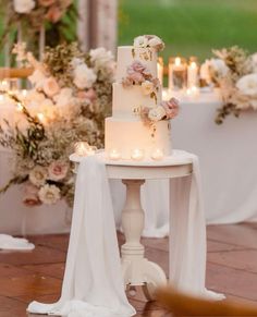 a white wedding cake sitting on top of a table with candles and flowers around it