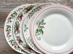 four plates with holly designs on them sitting next to each other in front of a wooden table