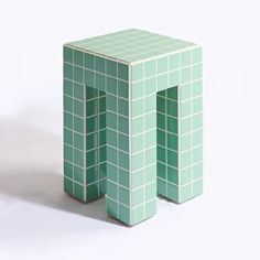 an odd shaped table made out of green tiles on a white background with one leg bent down