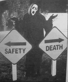 a black and white photo of a person wearing a scary mask standing next to two road signs