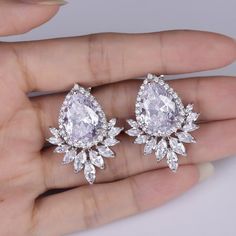 a pair of diamond earrings in the palm of someone's hand