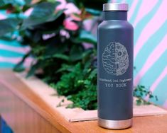 a stainless steel water bottle sitting on top of a wooden table next to green plants