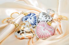 three different colored ornaments are on a white satin surface with gold accents and chains hanging from them