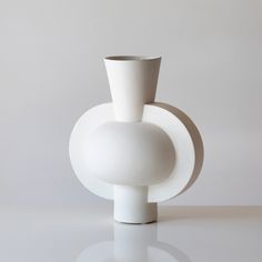 a white vase sitting on top of a table next to a gray wall and floor