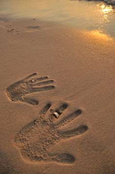 two footprints in the sand near the water at sunset or sunrise, with one person's hand and foot prints on the beach