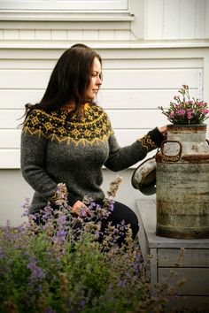 a woman sitting on a bench next to a vase with flowers in it and wearing a knitted sweater