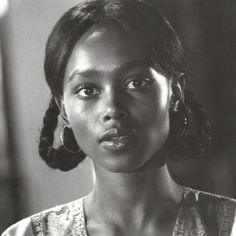 a black and white photo of a woman with large hoop earrings on her head, looking at the camera