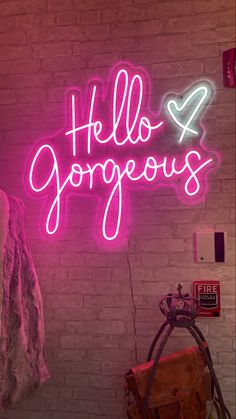 a pink neon sign that says hello gorgeous on the side of a brick wall next to a purse