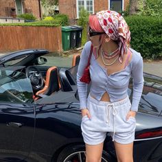 a woman standing in front of a car wearing shorts and a bandana on her head