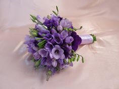 a bridal bouquet with purple flowers on a white cloth covered bed sheet, close up