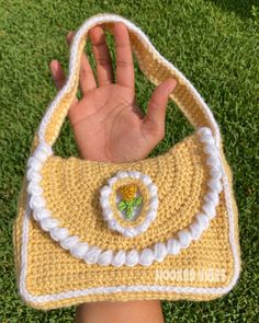 a hand holding onto a crocheted purse on top of green grass in front of someone's hand