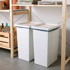 two white trash cans sitting next to each other on top of a wooden shelf in a room