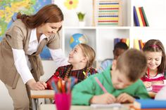 a woman standing over a group of children at a desk with pencils in front of them