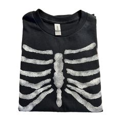 This punked-out tee is a wardrobe must for the angsty rebel in all of us. The gray and white skeleton rib cage graphic resembles an X-ray across the chest in a vivid print. The flexible fabric paint allows the rib cage design to move with you and lends a luxe, artisanal look. Whether you're moshing at a gig or snarling at the mainstream, this punk rock tee lets shows your nonconformist spirit. The soft cotton blend keeps you cozy during all-night thrash sessions, while the relaxed fit offers roo Bleach Rib Cage Shirt, Skeleton Rib Cage Jacket Bleach, Rib Cage Design Shirt, Ribcage Shirt, Rib Cage Shirt, Distressed Fitted Punk T-shirt, Rock Skeleton, Skeleton Rib Cage, Gothic Style Clothing