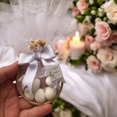 a hand holding a glass container filled with white balls next to a bouquet of flowers