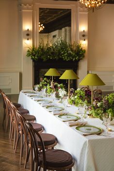 a long table is set up with place settings and green lamps on the wall behind it