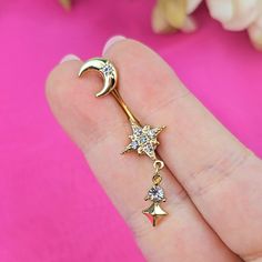 a close up of a person's hand holding a gold star and moon navel ring