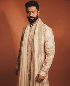 a man with a beard wearing a white suit and shawl standing in front of a brown background