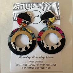 a pair of black, white and red earrings with gold accents on top of a card