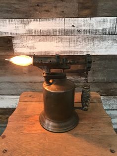 an old fashioned coffee grinder with a light on it's side and wood planks in the background