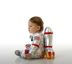 a baby sitting on the ground in a silver suit with an american flag painted on it