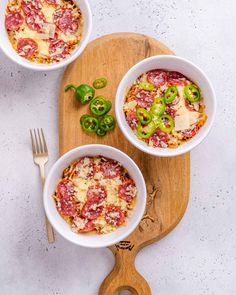 two white bowls filled with pizza on top of a wooden cutting board next to a knife and fork