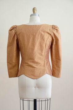 A homemade golden tan jacket, with puffed shoulders, gold faceted buttons, and good tailoring. It is unlined and light enough to be worn as a blouse. ☛ m e a s u r e m e n t s ☚ Bust: 32 Waist: 28 Shoulders: 13.5 Length: 21 ☛ d e t a i l s ☚ Era: 1990s Material: polyester Condition: excellent ☛ v i s i t t h e s h o p ☚ https://etsy.me/2Nd23kg ☛ instagram ┇ poppycockvintage ☛ facebook ┇ poppycockvintage Gold Fitted Blazer For Fall, Fitted Gold Blazer For Fall, Classic Fitted Gold Blouse, Fitted Gold Top For Workwear, Fitted Gold Tops For Work, Vintage Gold Blazer For Fall, Fitted Vintage Gold Blouse, Vintage Gold Fitted Blouse, Fitted Gold Vintage Blouse