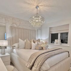 a large white bed sitting under a chandelier in a bedroom next to a window