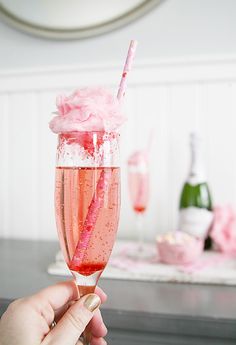 a person holding up a pink drink in a wine glass with a straw sticking out of it