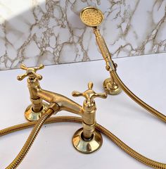 two brass faucets on a marble countertop with gold colored hose connected to them