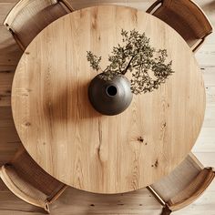 an overhead view of a round wooden table with chairs and a vase on the top