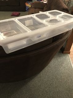 three plastic containers sitting on top of a brown ottoman in a living room next to a couch