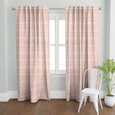 a white chair sitting in front of a window with curtains hanging on the windowsill