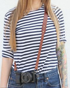 a woman wearing a black and white striped shirt with a brown leather camera strap around her waist