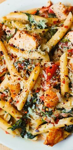 a white plate topped with pasta and chicken covered in sauce, parmesan cheese and other toppings