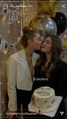 two women standing next to each other in front of a cake and balloons with the words happy birthday written on it