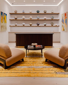 a living room with two chairs and a coffee table in front of a shelf filled with seashells