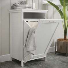 a white cabinet with towels in it next to a potted plant