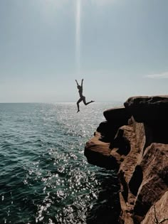 a person jumping off rocks into the ocean