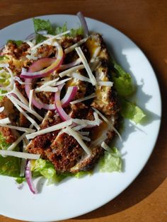 a white plate topped with lettuce and meat covered in cheese on top of it