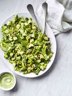 a white bowl filled with lettuce and avocado next to two spoons