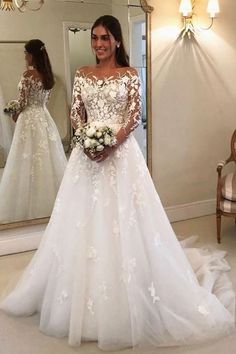 a woman standing in front of a mirror wearing a white wedding dress with long sleeves