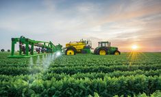 a tractor spraying water on a field with other farm equipment in the background at sunset